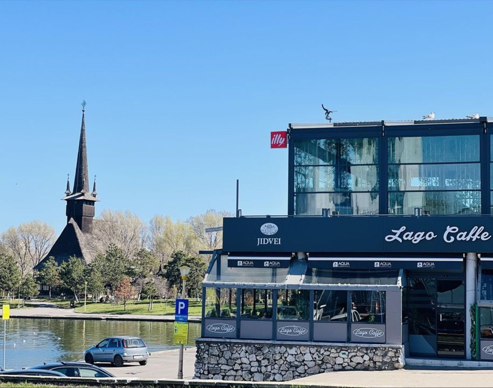 Clădirea Lago Caffe pe malul lacului Tăbăcărie, cu biserica de lemn din parc în fundal