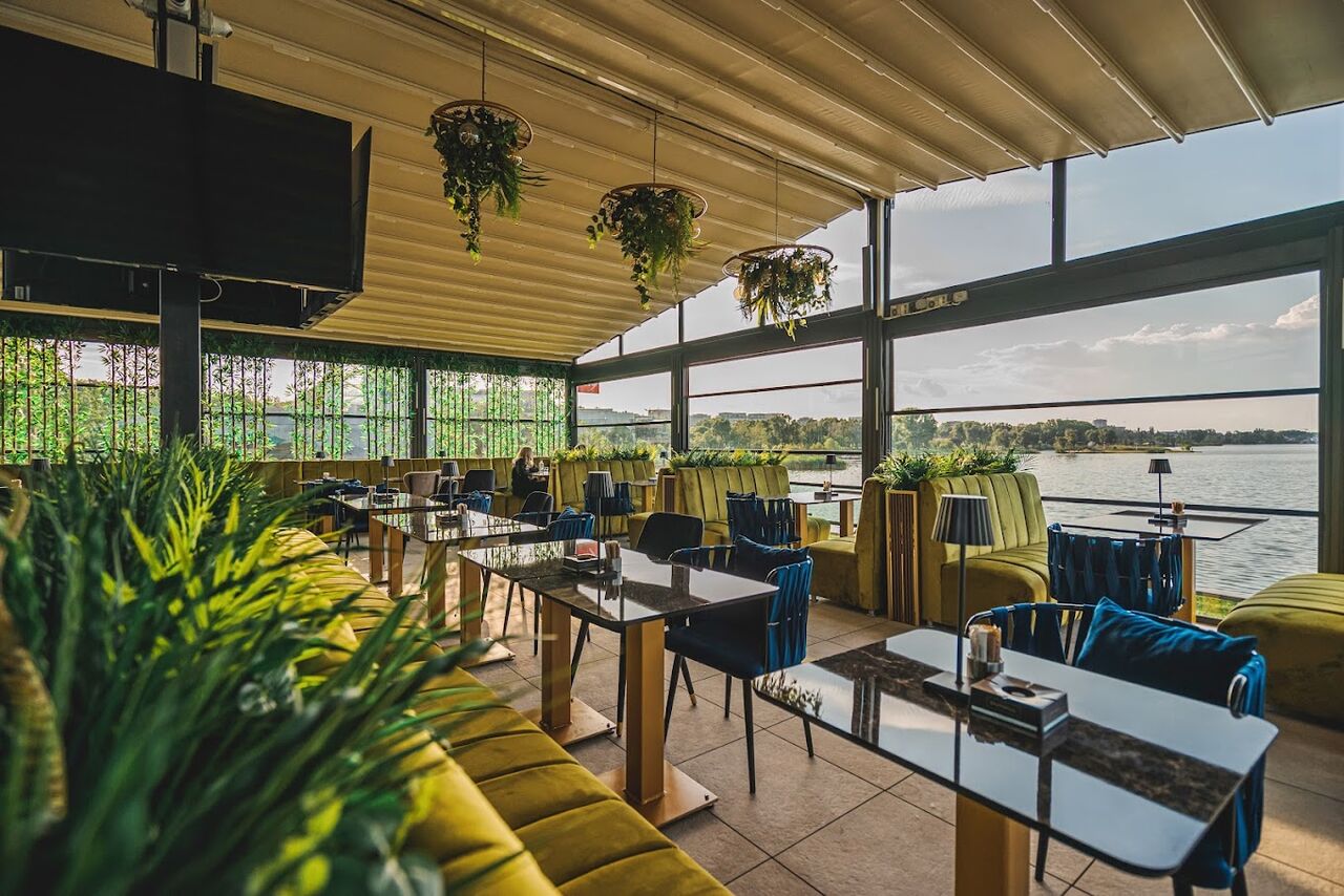 Salonul vitrat Lago Caffe, cu canapele galbene, scaune albastre și lacul Tăbăcărie în ferestre