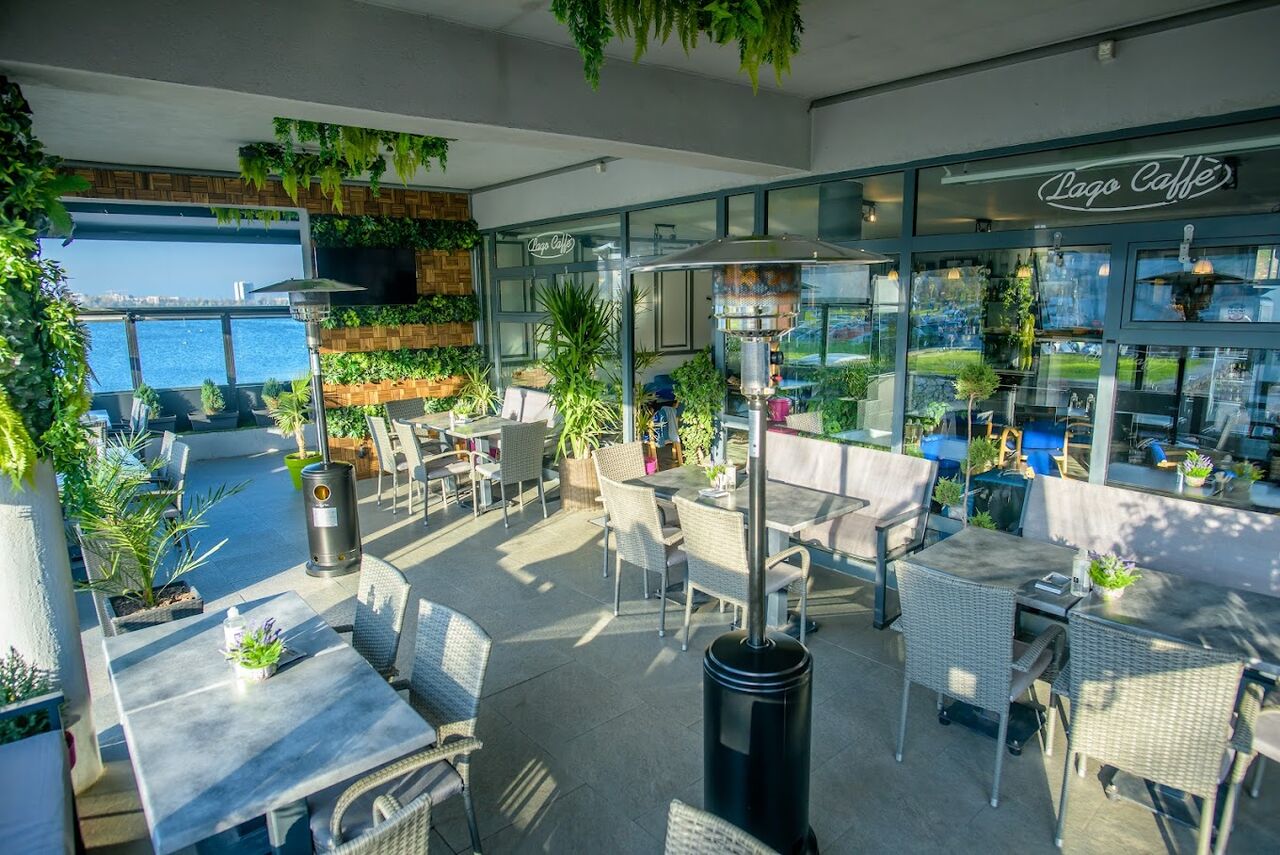 Terasa acoperită Lago Caffe, cu verdeață, mese gri și încălzitoare, în lumina după-amiezii